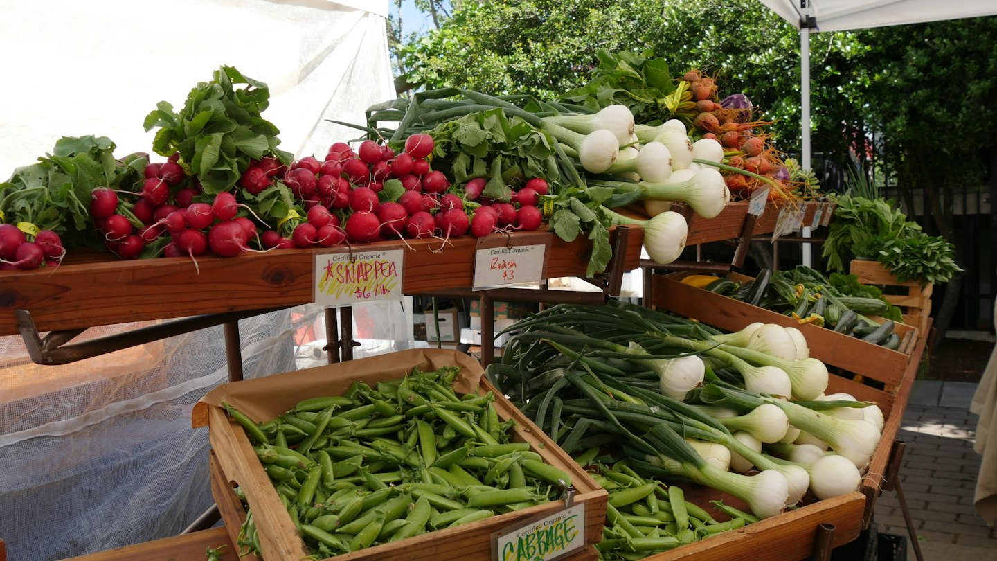 Outdoor market stall with fresh organic radishes, spring onions, and snap peas.