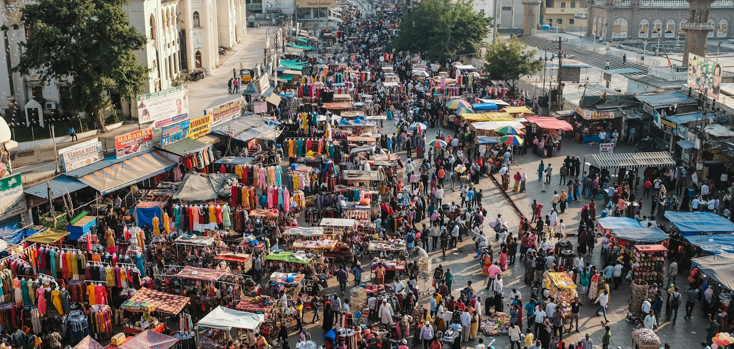 Crowds shop and walk through a vibrant outdoor street market.